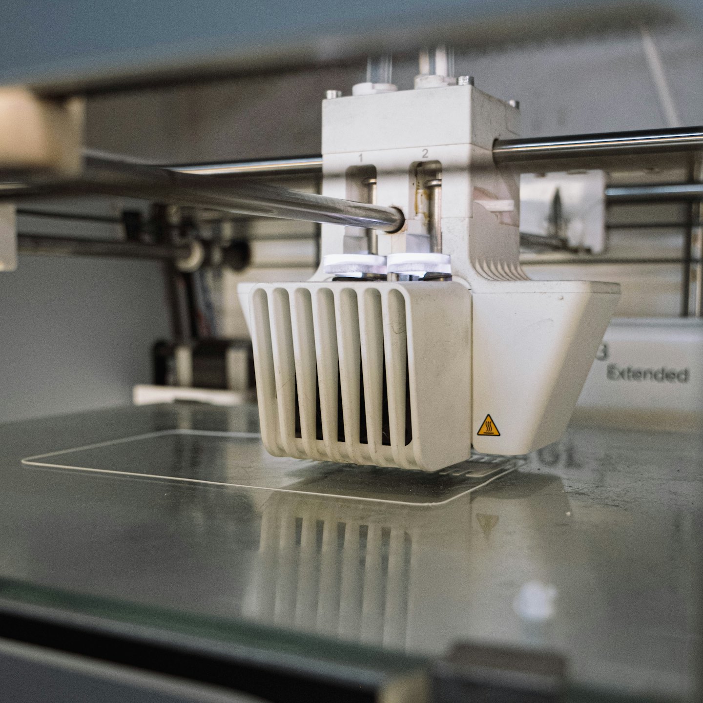 3D printer extruder head laying down transparent filament on glass.